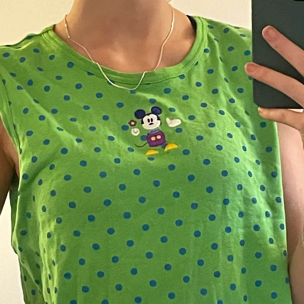 En grön arm-lös tröja med blå prickar. Cool icon på framsidan av Musse pigg. Cool att styla. Kommer från en Disney Store men jag köpte den second hand i Lund. . T-shirts.