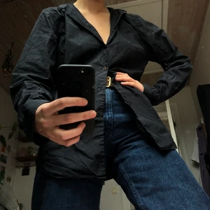 Svart skjorta  - Svart skjorta från J.LINDEBERG i toppkvalite. 100% bomull. Ganska rak mansmodell från början men funkar självklart unisex. Lite brunaktiga knappar som visas på sista bilden. 