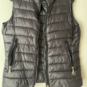 Väst från Mango  - En svart halv glansig väst från mango storlek M. Två fickor i ett bra skick. Köpt för 2 år sen ungefär och inte använd alls mycket. 