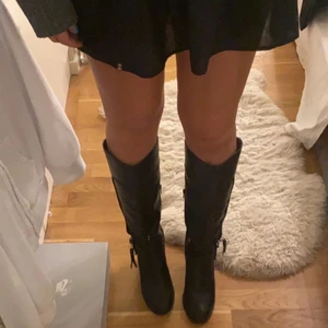 Höga boots i klack - Säljer dessa höga boots i svart läder med böj på toppen och snygga detaljer. Näst intill oanvända. Storleken är 39 men skulle säga att de även passar 38. Priset är exklusive frakt. Kram💕