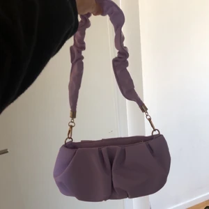 Liten lila väska - Jättefin lila liten axelväska i nyskick! Aldrig använd. Super fin lila färg med guldiga detljer. 