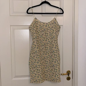 Figursydd tajt klänning - En gul figursydd klänning med blå och lila blomdetaljer, sitter fint med smala axelband. 