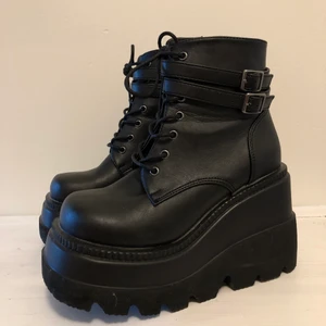Demonia shaker-52 - 11,4 cm staplade wedge plattform Lace-up front fotled boot med dubbla Bucklad fotled remmar, inside blixtlås stängning. Vegan vänligt läder. Köpte dom från dollskill för 1200kr. Skorna är endast använda 1 gång utomhus. Säljer dom nu pga kommer ej till användning längre. Dom är sköna och enkla att gå i. 