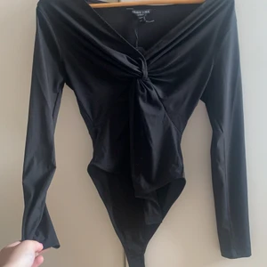 Svart body - En snygg svart body med en fin detalj vid v-ringningen. ALDRIG ANVÄND, prislapp kvar. Storlek XS