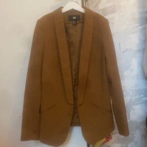 Mockafärgad kavaj HM Strl 34 - Otroligt snygg mockafärgad kavaj från HM i Strl XS. Aldrig använd! Stum i tyget, alltså INTE stretchig. Fejkade fickor fram. Ingen möjlighet till knäppning. Gjort i klassiskt ”kostymtyg”! 