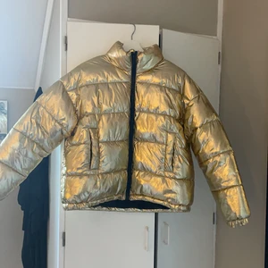 Guldig pufferjacket från Monki - En asball pufferjacket från Monki i storlek M. Haft till vardags och även i samband med skidresor. Säljer då jag ej får användning för den längre. 