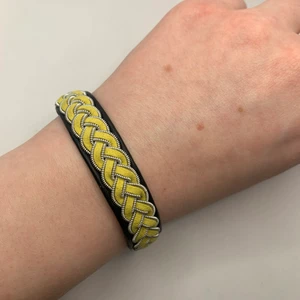 Tenntrådsarmband  - Handgjort Tenntrådsarmband, svart med gul fläta. Materialet armbandet är gjort i är lammskinn, och flätan är gjort i tenntråd. Armbandet kan hålla i flera år. Om du har någon fråga kan du gärna skriva en kommentar eller meddela mig.