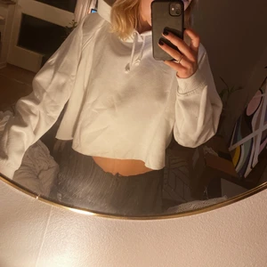 Vit croppad hoodie - Vit croppad hoodie från BIKBOK. Använt men gott skick. Modellen ser avklippt ut men den ska vara så, det är en söm längst med kanten. Storlek XL.