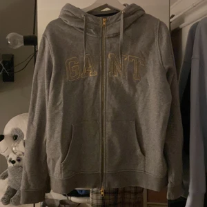 Grå Gant Hoodie med guld detaljer  - En grå Gant Hoodie med guld detaljer. Endast använd ett fåtal gånger och är i bra skick. 
