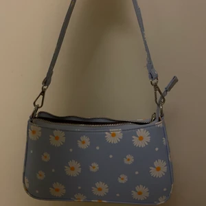Blåblommig axelväska - Axelväska i ljusblå med vita och gula blommor på, man kan ta av och på axelbandet och insidan har flera fack