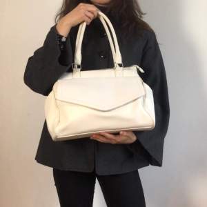 En vit handväska i skinn imitation. Krokodilmönster på ”flärpen” på framsidan av väskan 