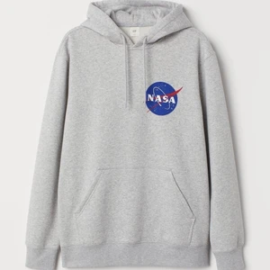 Huvtröja med tryck NASA - En huvtröja i sweatshirtkvalitet med tryck. Tröjan har trikåfodrad huva som är omlottlagd fram och har dragsko. Lång ärm och känguruficka. Ribbad mudd vid ärmslut och i nederkant. Mjuk, borstad insida.