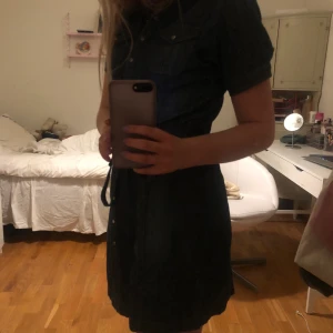 Mörkblå Jeansklänning - Mörkblå jeansklänning med knappar och knyte i midjan, går ungefär till knäna, stor storlek men passar mig som vanligtsvis har en S utmärkt💙 bara att skriva vid önskan av fler bilder! Köparen står för frakt 