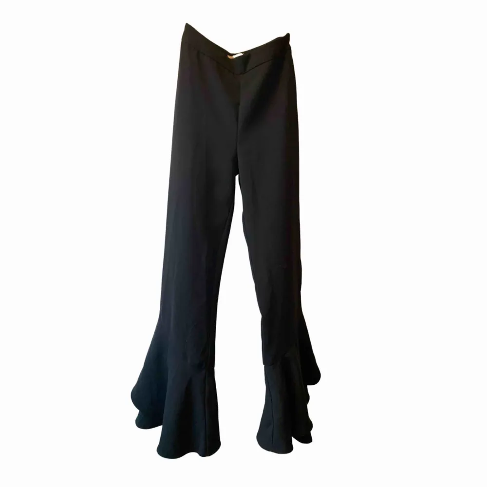 Ett par svarta kostymbyxor med volanger längs ner på benen! Supersnygga att ha för att lyfta en outfit och sitter väldigt smickrande på kroppen. Storlek XS👊🏻✨. Jeans & Byxor.