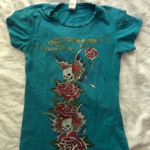 Ed Hardy t shirt!!! - Säljer nu denna jättefina klarblå Ed Hardy t-shirt! Den är köpt second hand men i bra skick, doxk har stenar gått av från trycket som går att se på bild 2. Står inte storlek men skulle gissa S/XS då den sitter ganska tight. Budgivning om fler är intresserade! Möts upp i Sthlm eller fraktar 💘