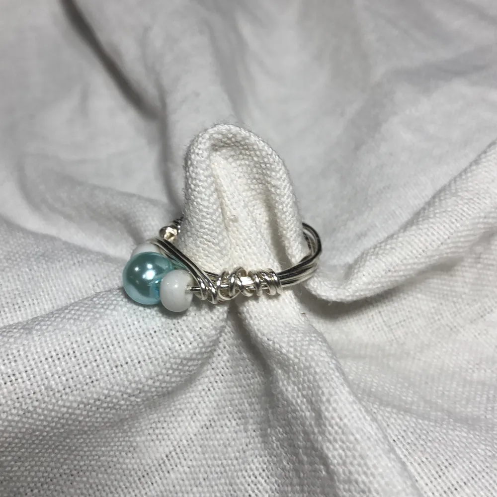 En hemmagjord ring med två små vita pärlor och en stor ljusblå pärla. Passar bra till mycket. 70kr med frakt!🚚. Accessoarer.