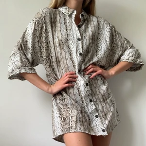 Skjorta / klänning från Pull and Bear  - En lång skjorta / klänning med ormmönster från pull & bear i strl S. Superskönt tyg som gör den perfekt att bara slänga på sig över bikinin till stranden eller klä upp med klackar till middagen. Använd ytterst få tillfällen så i princip som ny. FRAKT tillkommer från 66kr. 