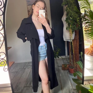 Svart kappa i 100% polyester från BIKBOK  - Är i storlek L men kan även passa storlek S! Är förövrigt normal i passform och i storlek. Plagget saknar ett band att knyta åt runt midjan, men man kan använda till exempel ett skärp som jag har på bild två! 200kr +frakt! 