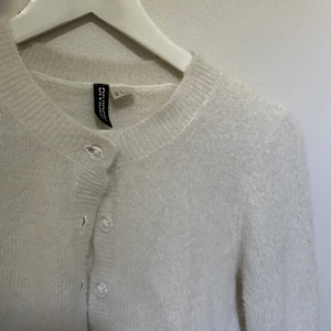 Vit ”fluffig” kofta från H&M strl S - I fint skick, säljer då jag inte använder den tillräckligt! Den är croppas och har genomskinliga knappar på framsidan. Perfekt nu till hösten då det blir lite kallare! 