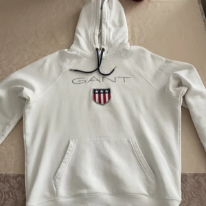 Gant Hoodie i färgen Vit - En Gant Hoodie med ordinarie pris på 1099kr. Den är använd ganska mycket, den har även lite små fläckar vid mag delen, annars är den i okej skick!