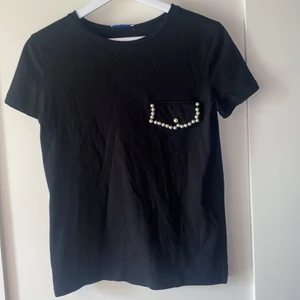 Tshirt  - Svart tshirt som har en fakeficka med pärlkant