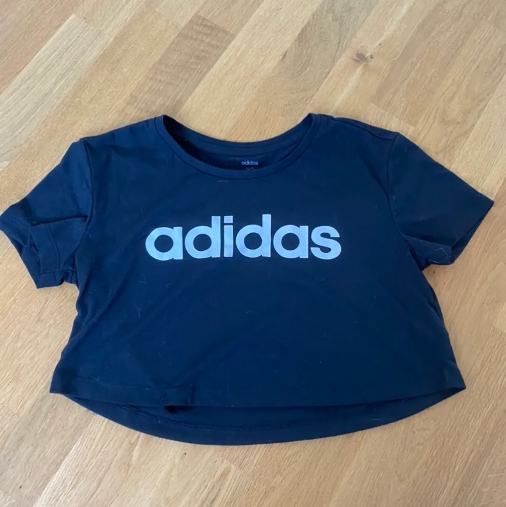 Fin croppad t-shirt från adidas i storlek XS, är svart i verkligheten (ser bara blått ut på bilden för ljuset blev skumt), använd typ 2 gånger så är i väldigt fint skick🥰 60kr + frakt💞. T-shirts.