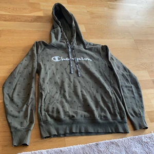 Champion  - En grön champion hoddie med små champion logan som mönster 