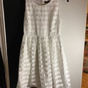 Klänning - En vit knälång klänning, med randigt mönster. Den är i storlek 38 använd endast fåtal gånger 