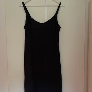 Klänning - Svart klänning som går ner till knäna med en liten slits på varje sida 