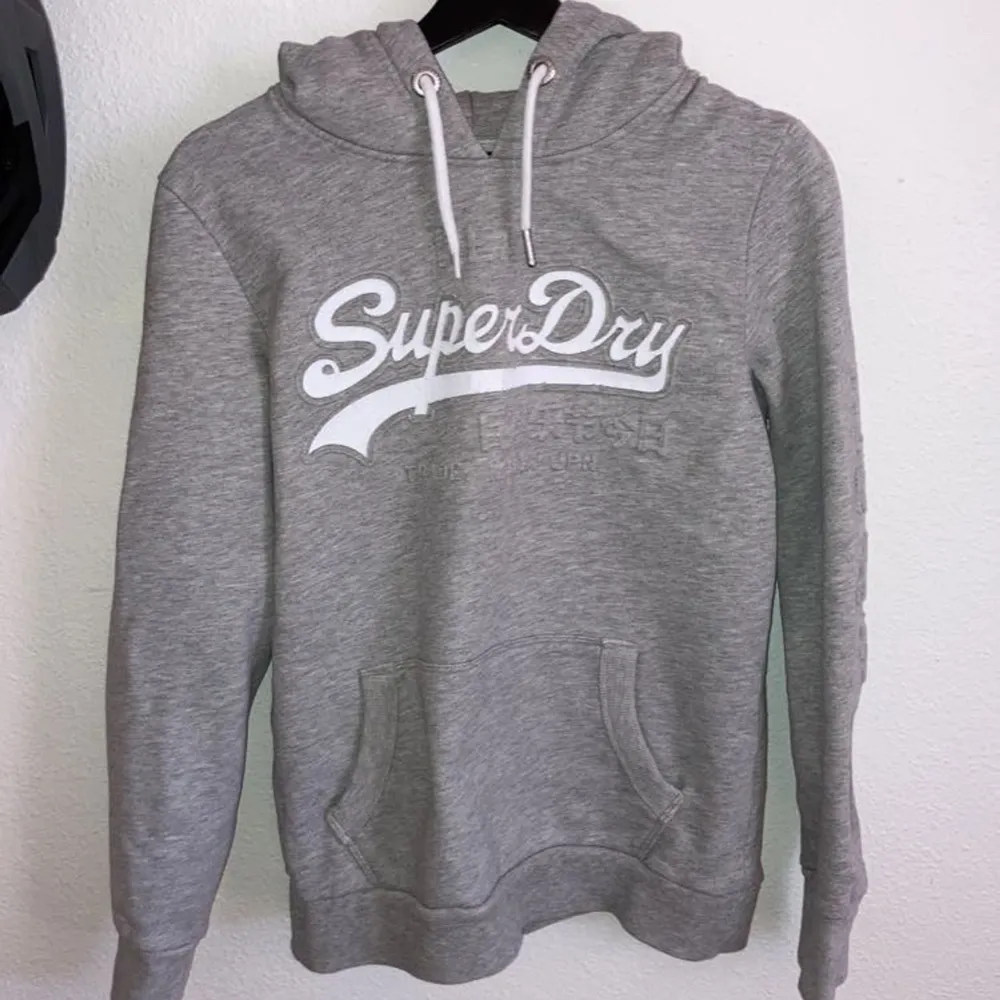 Grå superdry hoodie storlek M med superdry tryck på framsidan. Hoodien har även japanska bokstäver på ena ärmen. Skulle säga att den är lite liten i storleken. Använd men i bra skick.. Hoodies.