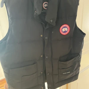 Canada Goose Väst - Canada goose väst i storlek L, köpt några år sen, inte använd pågrund av storleken. Inga hål eller något men lite damm kanske för den har bara hängt och inte används. ÄKTA!