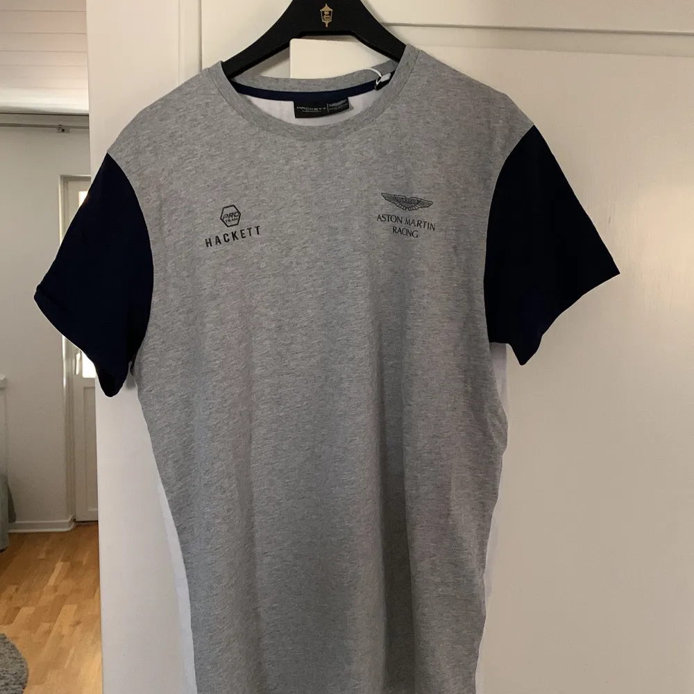 Fin och fräsch t-shirt från Aston Martin Formel 1 merch. Från märket Hackett som är känd för högkvalitativa kläder. Vit på baksidan och grå på framsidan, storlek M, något mindre än en vanlig medium. T-shirts.