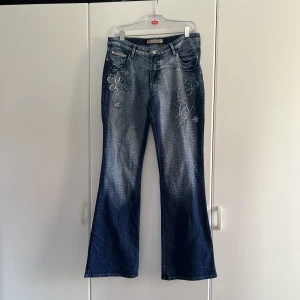 Jeans med pärlbroderi - Jättefina lågmidjade jeans med ljusblå pärlbrodering av blommor längs höfterna, även på baksidan på fickorna 💙Mörk och kall wash (Första och sista bilden visar färgen bäst) 🧚‍♂️ Bootcut 🦋Vintage märke: You yi pim. Midjemått (tvärs över): 42 cm