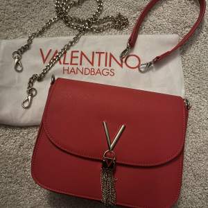 Ny valentino väska, röd med gulddetaljer. Finns både läderrem för att ha den som handväska men också en guldkedja för att ha den som axelremsväska. Dustbag medföljer. 