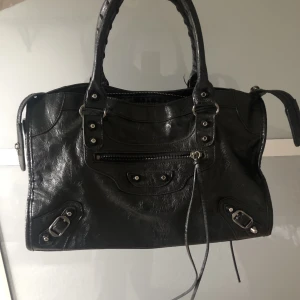Handväska - Trendig handväska i läderimitation i gott skick.  Liknande Balenciaga väska. Har ett fack på utsidan och ett på insidan. Tillkommer ett längre band. Inga märken eller defekter! Bredd;38 cm Höjd;22 cm Djup;15.