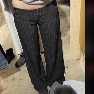 Kostymbyxor - Säljer dessa lågmidajde kostymbyxor köpta på beyond retro med gula små ränder, ser vita ut och snygga knappar. Aldrig använda av mig. Står ingen direkt storlek men passar mig som är 174 cm och har storlek 36-38 i jeans. Kontakta mig för fler bilder 