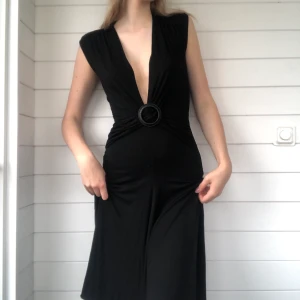 Klänning - Svart klänning med en djup v ringning. Går ända ned till knäna (bild 3). Sitter åt midjan med hjälp av skärpet  Fraktkostnad tillkommer 