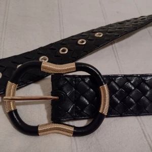 Oanvänt svart bälte/skärp i äkta skinn, med stort spänne och guldfärgade detaljer, 80 cm - Oanvänt svart bälte i äkta skinn med ett stort spänne med guldfärgade metalldetaljer. Galet snyggt men har inte kommit till användning här. 80 cm långt och ca 4 cm brett.