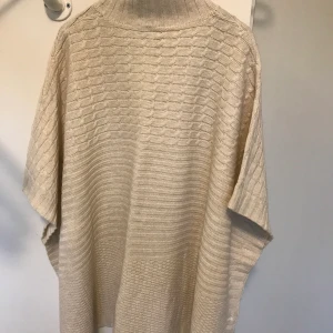 Väst/poncho - Fin naturvit stickad bäst/poncho med polokrage. Från Divided H&M i stl M. Knappar i sidorna. Frakt betalas av köparen.