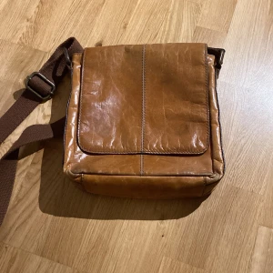 Brun läder axelremsväska - Säljer denna axelremsväska eftersom att den inte är min stil längre, brukade ha den hela tiden, men är fortfarande i bra skick! Mått: höjd: 30cm, bredd: 28cm