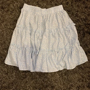 Ljusblå kjol - Ljusblå blommig kjol, helt oanvänd, storlek 36 men passar även en 34 och 38.