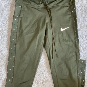 Nike tights M - Ett par militärgröna tights från Nike med fickor på båda sidorna och knytning i midjan. Jättesköna och sitter supersnyggt! De har även ett prickigt mönster längs sidorna i reflexmaterial. Tightsen är i storlek M och är true to size! Tightsen har även en ficka i midjebandet med dragkedja💚
