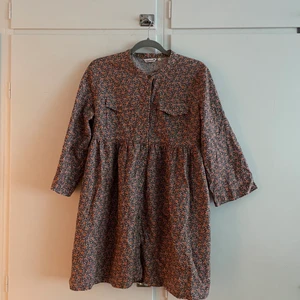 Blommig tunika/klänning - Supersöt klänning/tunika. Märkt typ 44/46 men jag som är s har använt den som klänning och sitter bra (m/l funkar nog). Har knappar hela vägen framtill men behöver en säkerhetsnål lämgst ner för att inte blåsa upp liksooom. Frakt ingår ej, hojta för pris!