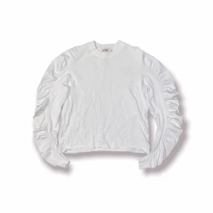 Volang tröja - Vit långärmad tröja med volang längst armarna från Carin Wester. 65% viskos 35% polyamid