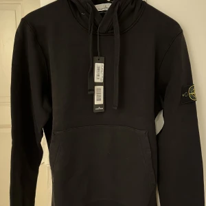 Stone Island hoodie - Svart Stone Island hoodie i storlek S, helt oanvänd med tags kvar nypris 2700. Köpt på Man of a kind för ungefär ett år sedan innan de slog ihop med NK. Inte använt för den blev för liten direkt o bara blivit liggande. Skriv för kvitto o fler bilder