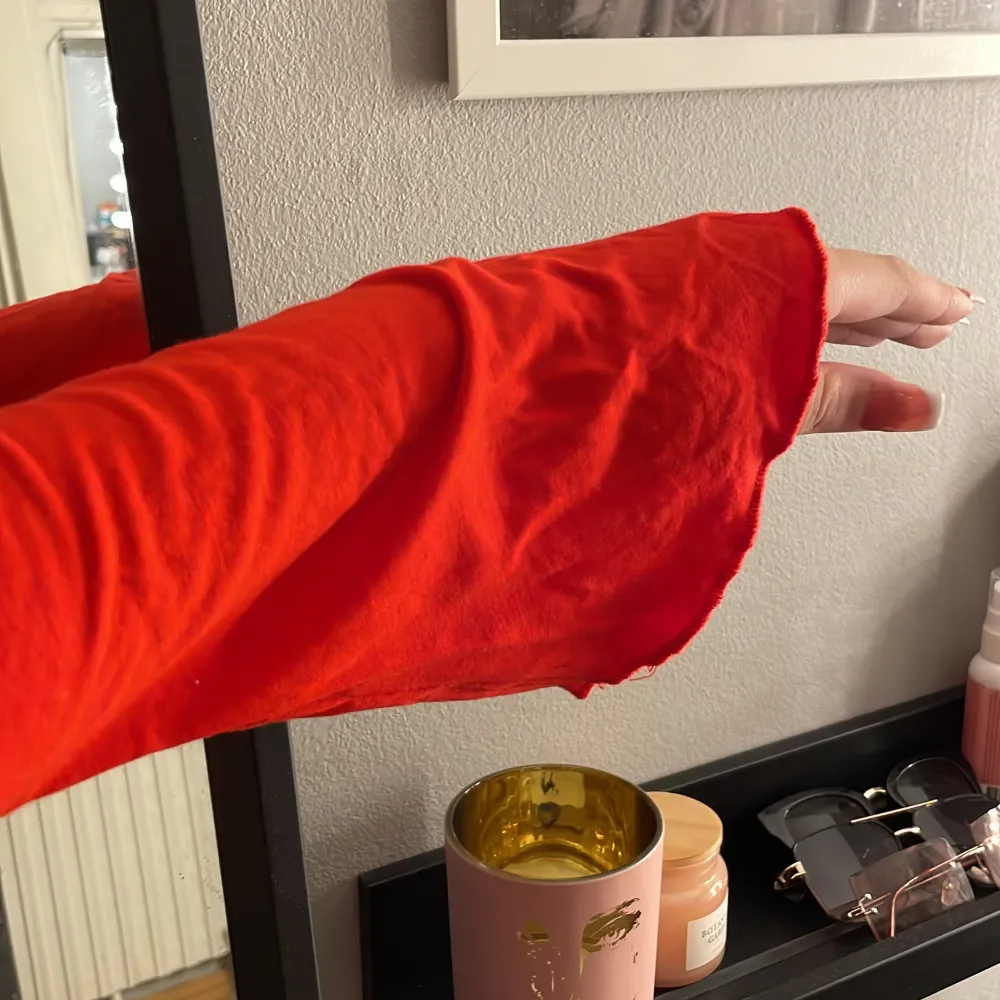 En röd Långarmad tröja som knappt andvänts samt att den har lite vidare armar vid händerna samt en vringning med en metal bit inuti . Toppar.