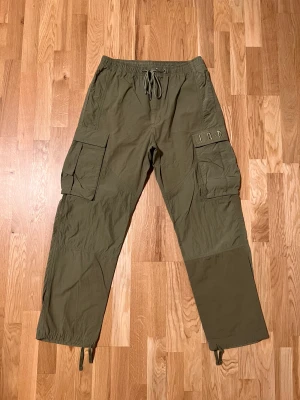 Jordan cargobyxor - Cargobyxor från Jordan i bomull och polyester detaljer. Stora praktiska fickor och riktigt bra fit då dem lägger sig fint över skorna. Köptes för på Zalando för retail: 999kr säljs nu för 400kr då de knappt är använda. Skick 9/10 inga defekter 