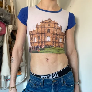 Blå vit brun grön babytee tryck byggnad text y2k 90s - Vintage babytee med blåa ärmar & krage och tryck av en byggnad på framsidan och text på baksidan 🏛🌿🌿 Älskar tryckets 90-tals vibe men också etiketten! <3