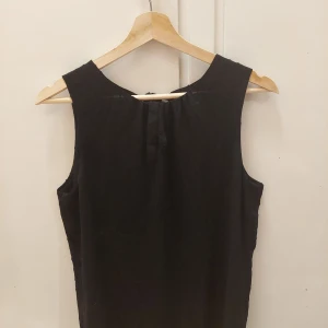 H&M, 38 - En ärmlös svart blus med små insydda prickar. Den är öppen i ryggen med två band som är är knutna i en rosett. Den är i bra skick. 60kr+frakt
