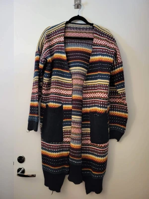 Lång stickad cardigan storlek M - mysig stickad cardigan med fint mönster och fickor. aldrig använd. Storlek M. Kan hämtas i Upplands Väsby eller i Gamla Stan efter 16 på vardagar.